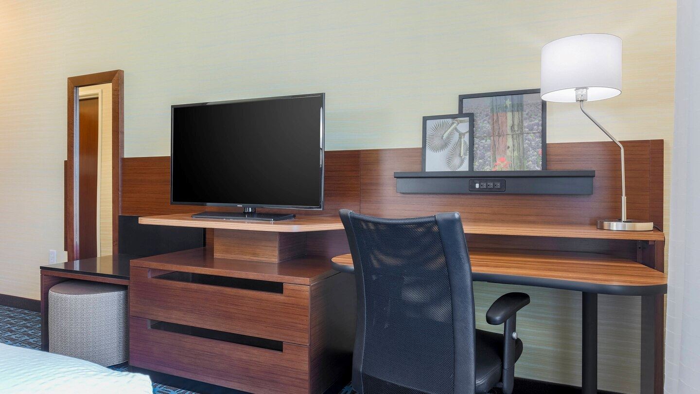 Guest room with wood vener work desk with a chair and tv