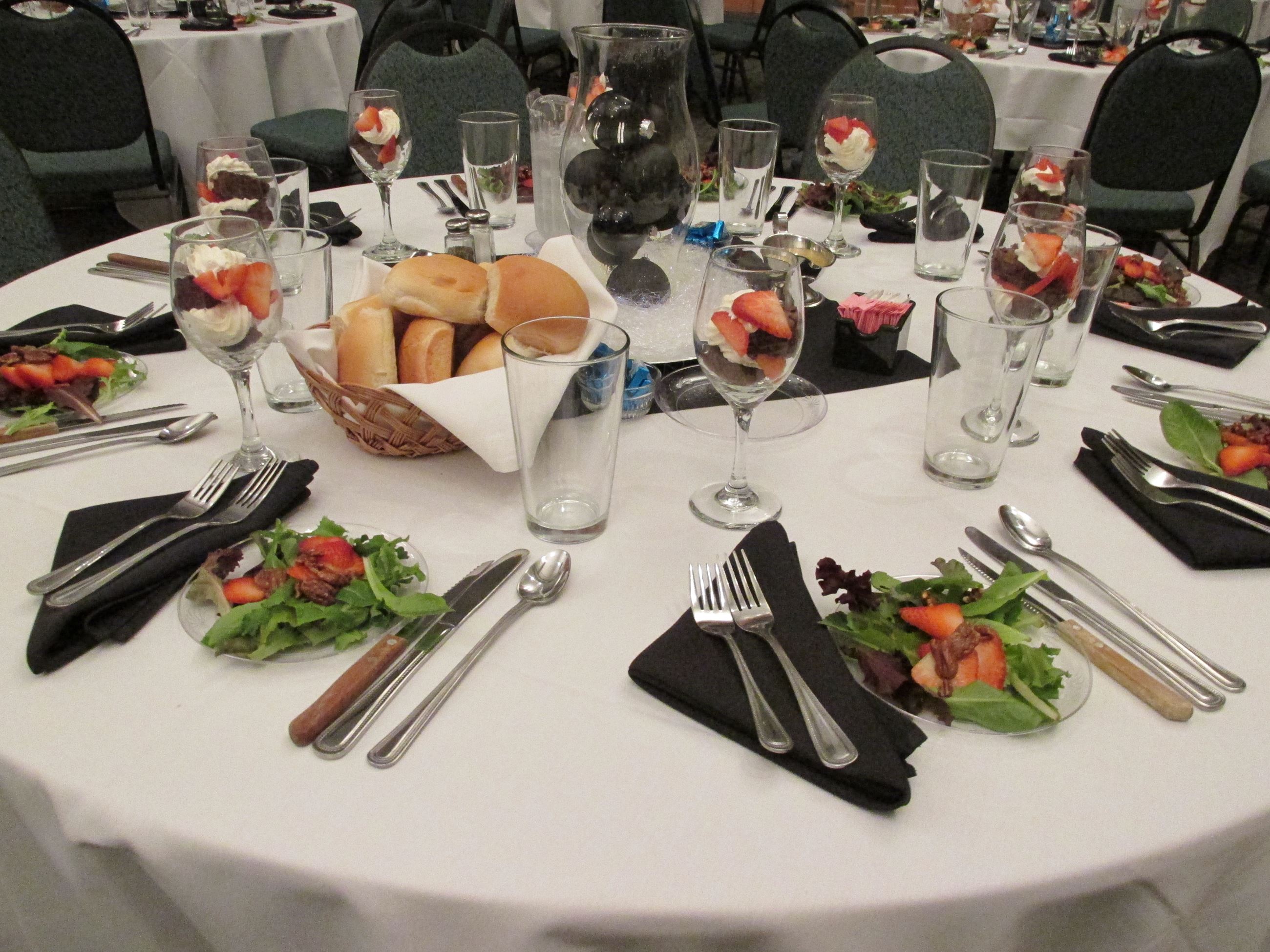 Pre-set tables with place settings and salads and rolls and parfaits in wine glasses